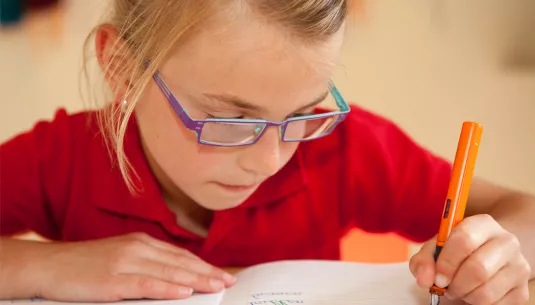 A girl with glasses writing in an exercise book