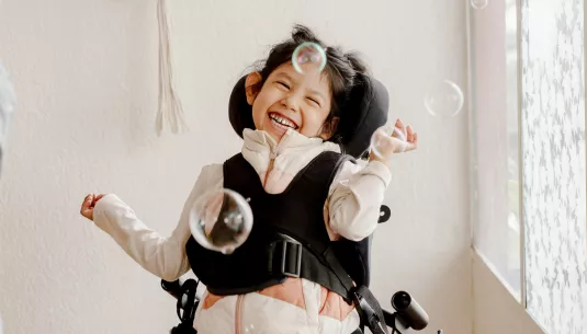 A girl in a wheelchair enjoying some bubbles in the air