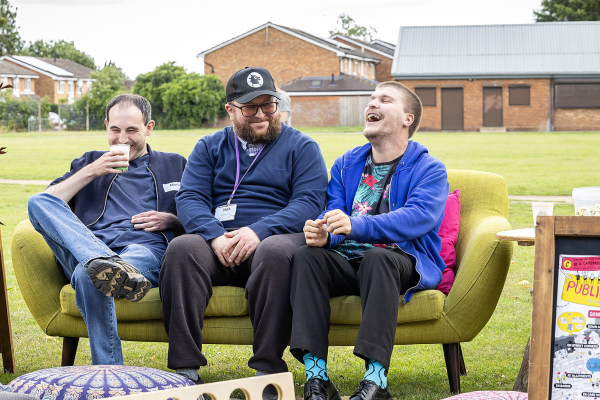 Three men sat on a sofa outside laughing together
