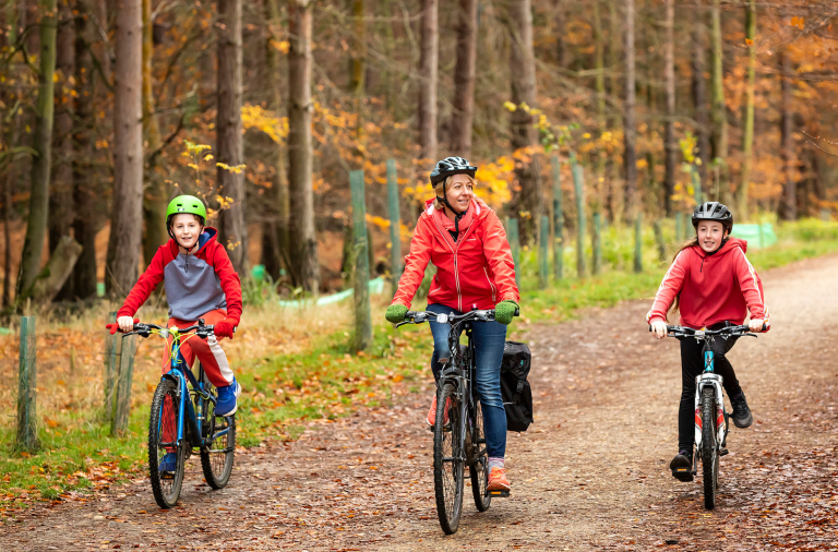 A woman flanked by her two children smile as they cycle down a country path in the autumn