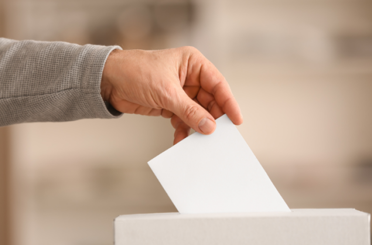 A hand over a ballot box, posting a ball