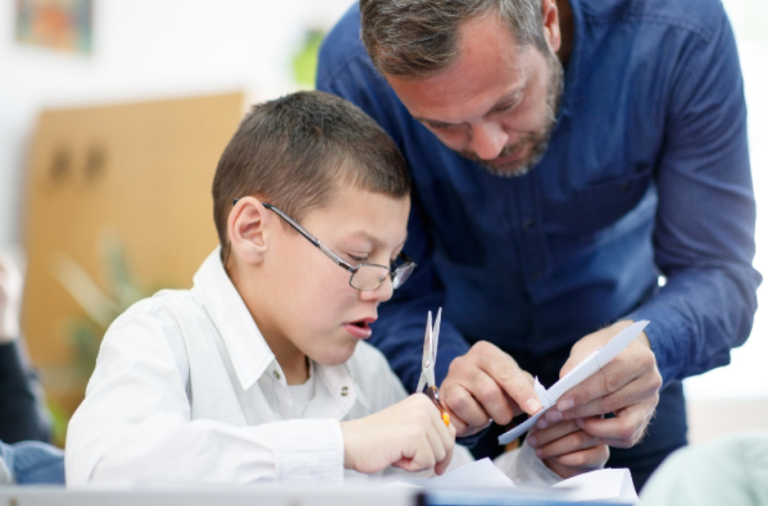 A teacher supports a boy with SEND who is sat at a desk at school