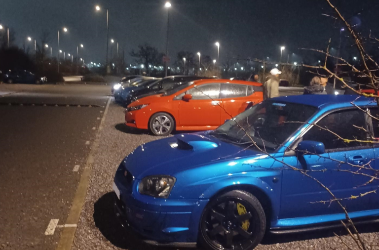 A row of cars lined up in a car park at night, under flood lighting