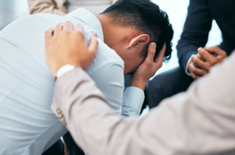 A man with his head in his hands is consoled by others