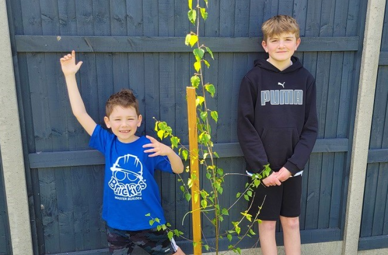 Two smiling boys stood with their newly planted tree in their garden
