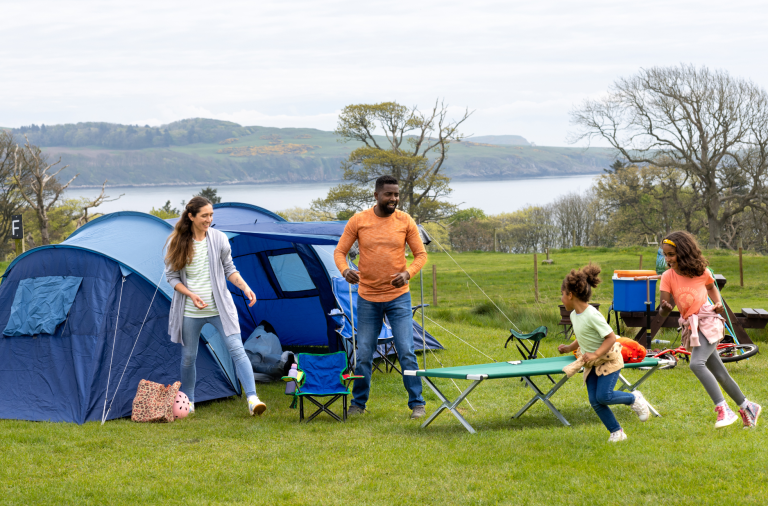 A family on lush green grass with children playing near their tent, close to the sea
