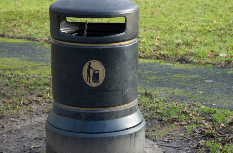 A litter bin next to a path with grass around