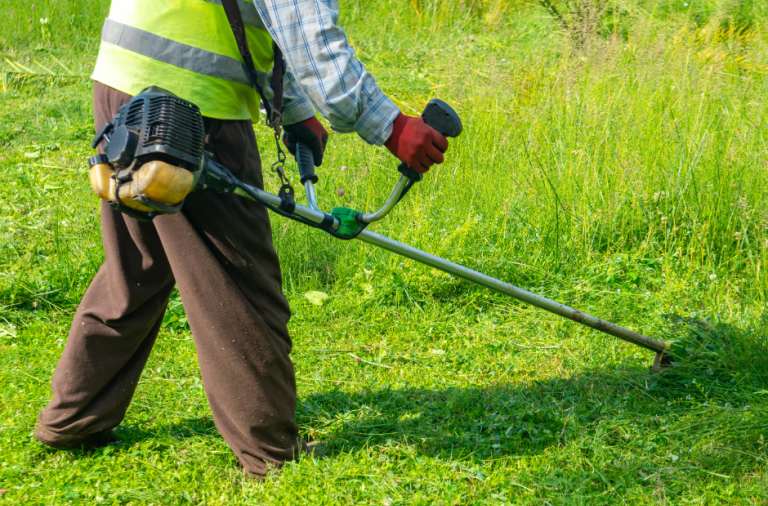 A worker wearing high vis jacket using a strimmer on grass