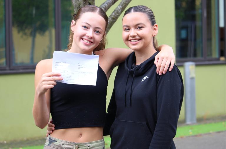 Two GSCE students posing with one has a result slip on hand