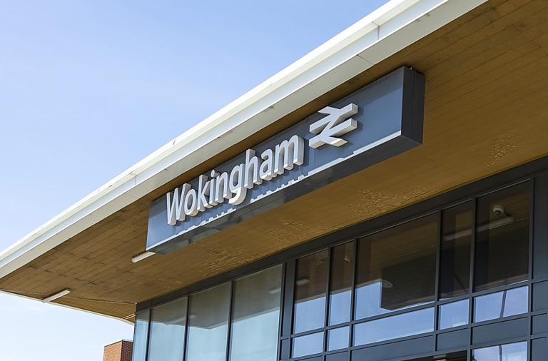 Two women walk past the main entrance to Wokingham train station on a sunny day