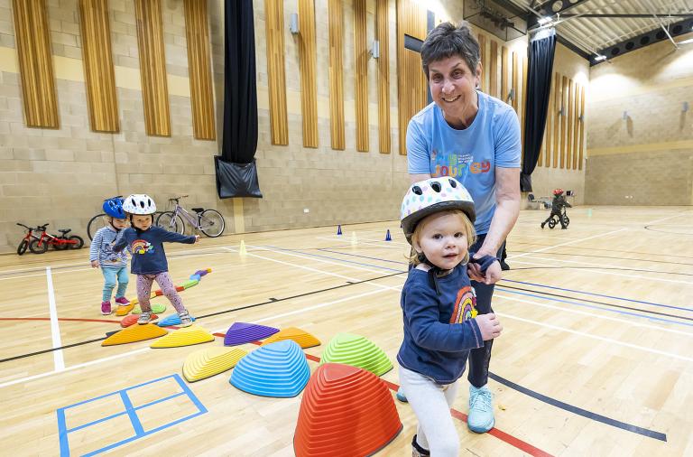 A woman smiles at the camera as she guides a very small child across a series of plastic stepping stones