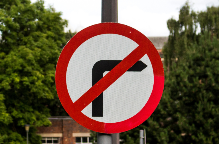 No right turn road sign on a pole with blurred trees and building behind