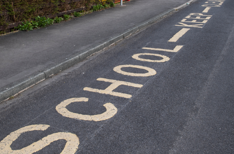 A road outside a school with school keep clear painted on it in yellow