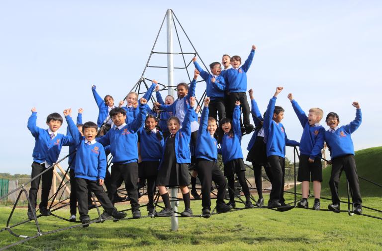 Young children in school uniform raise their fists and cheer while climbing up a large frame of ropes