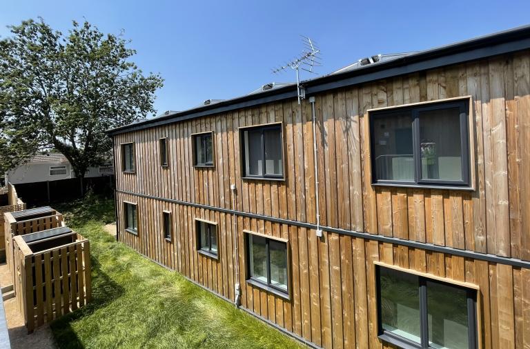 Photo of a two-storey timber clad, flat roofed temporary housing unit surrounded by grass