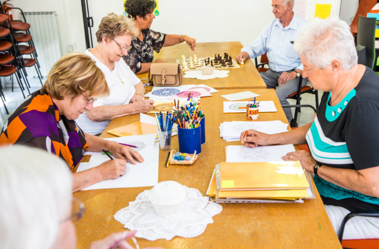 A group of older adults sat around a table doing a drawing class