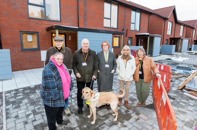 Six tenant volunteers and a guide dog stand outside a new row of council houses nearing construction