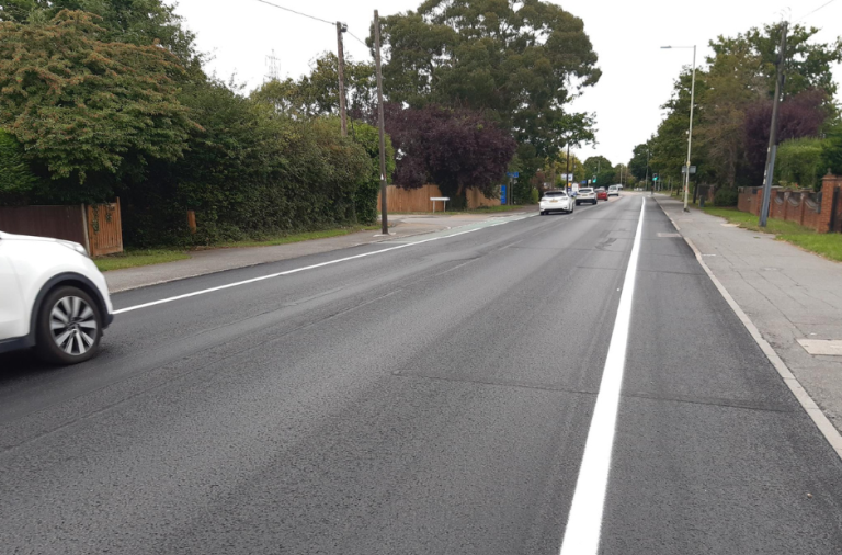 Part of a road that has been treated with asphalt preservation. Cars are seen driving along one side of the road.