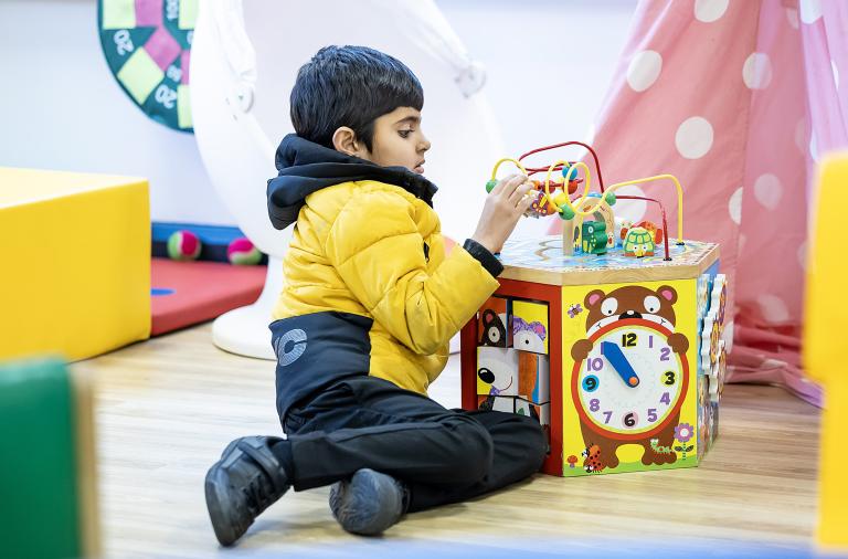 A boy sits on the floor of a classroom playing with an activity cube