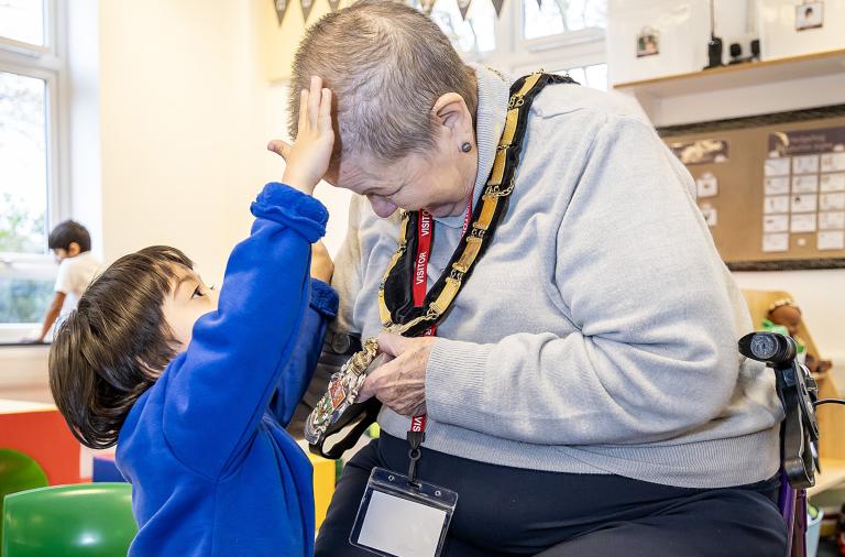 The mayor bows her head to a child who is enjoying stroking her hair