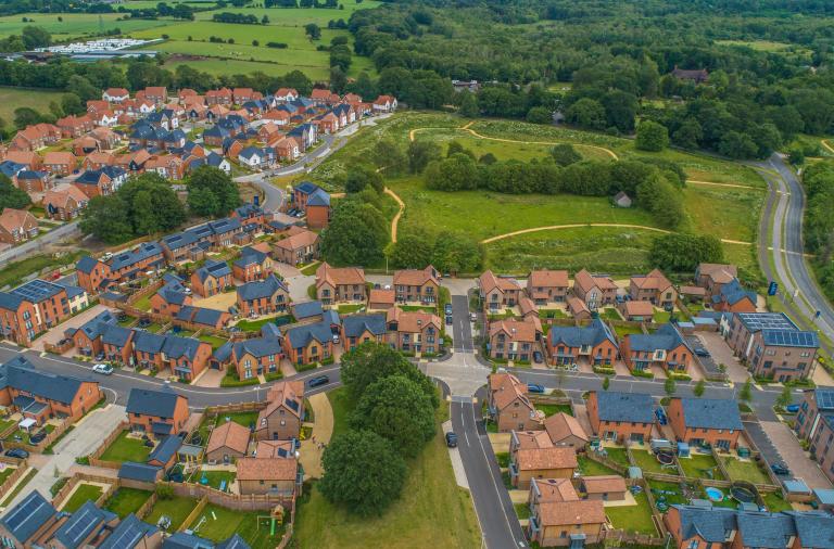 An aerial view of an area where new housing is being built, with large areas of green space and trees as well as parks with footpaths