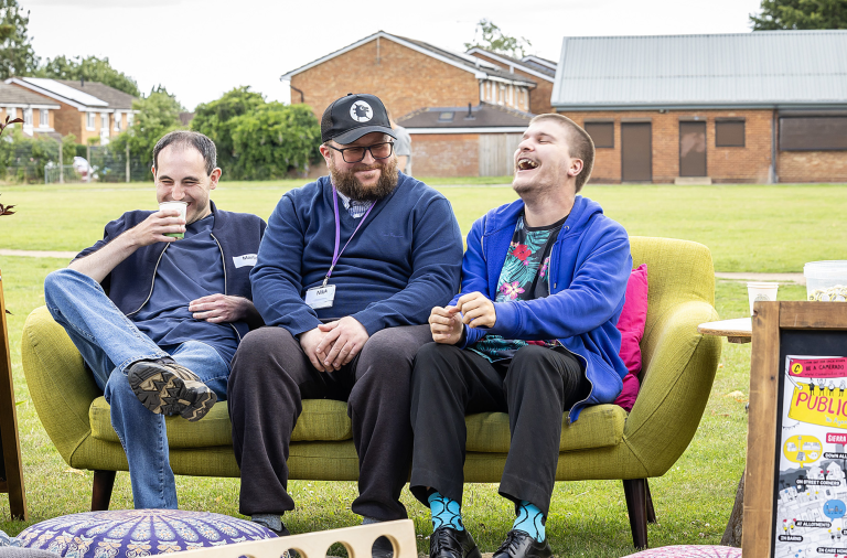 Three men sat on a sofa outside laughing together