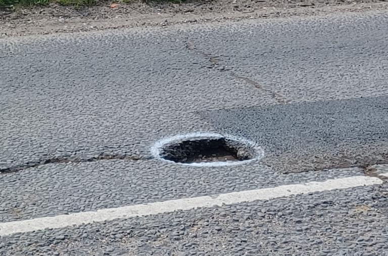 An image of a deep pothole in the middle of a main road