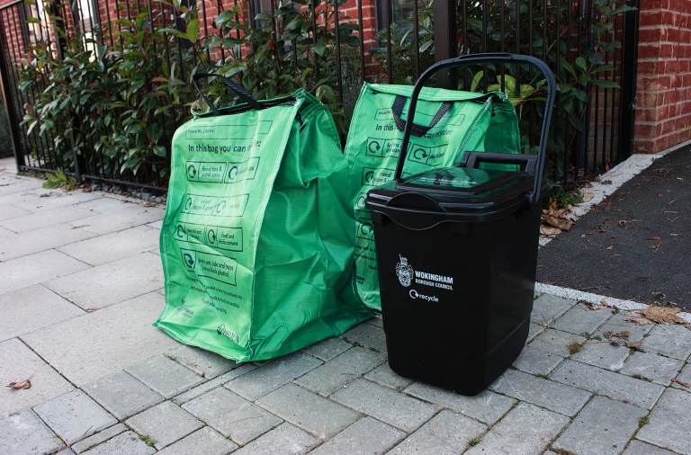 Photograph of two full green recycling bags and a black food waste bin at the kerbside in front of a house