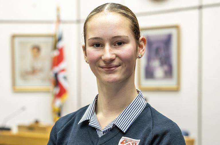 Maya smiles towards the camera while standing in the council chambers