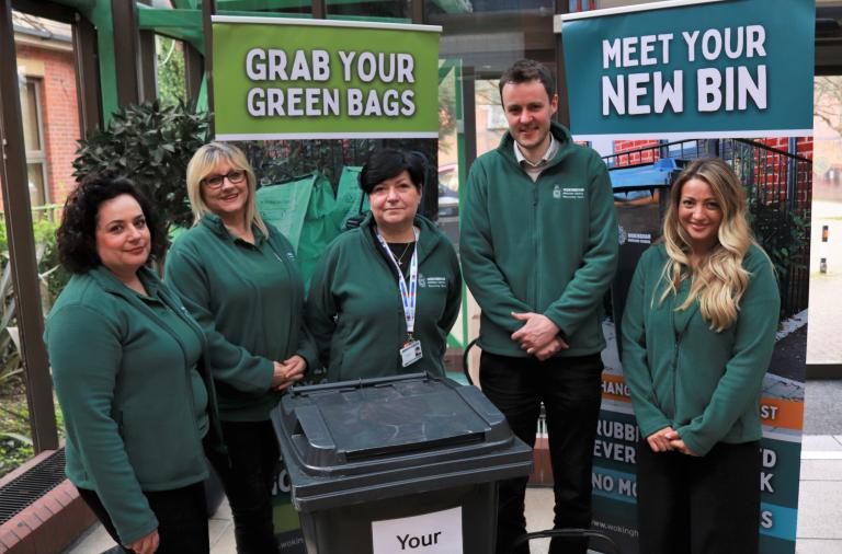 Four women and a man in dark green council jackets pose with a new black wheeled bin at the council's offices