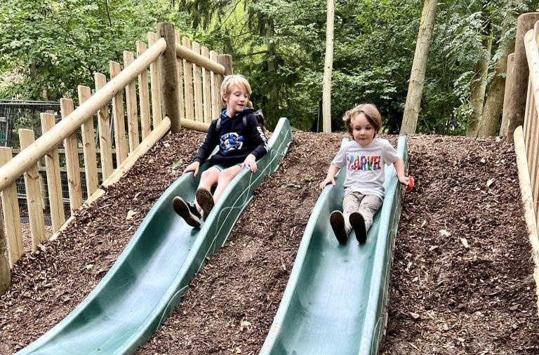 Two children beam with smiles as they go down slides at Camp Mohawk