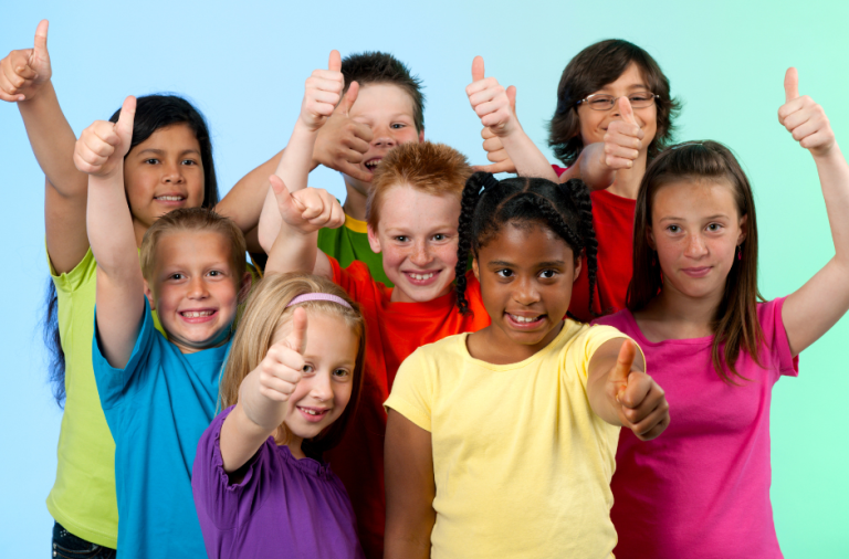 A group of eight children wearing brightly coloured tshirts smiling at the camera and giving a thumbs up