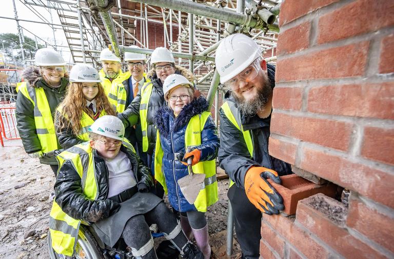 Daisy and her family lay a brick at their home in Gorse Ride. Also pictured is:  Barry Williams, project director at Wates Residential (back row centre); Cllr Stephen Conway, leader of the council and executive member for housing (back row right) and Katie Meakin, head of development – commercial property (back row left)