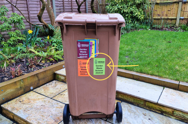 A brown garden waste bin with stickers in a garden
