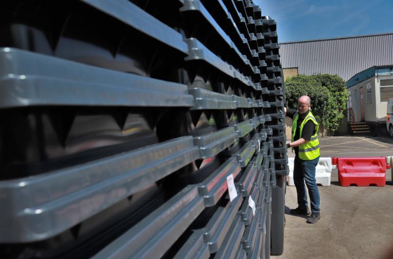 Close-up shot of a tall stack of bins as a man wheels another stack into shot in the background