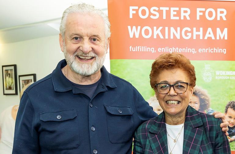 Havva and Jim smile to the camera in front of a 'foster for Wokingham' banner