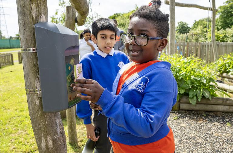 A child smiles at the camera while holding a contactless card up to a reader to win points