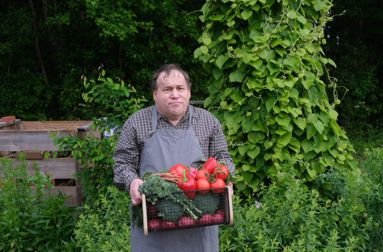 A man with autism carries a basket full of freshly picked vegetables in an allotment