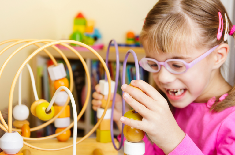 A young girl with SEND beaming while playing with a bead run