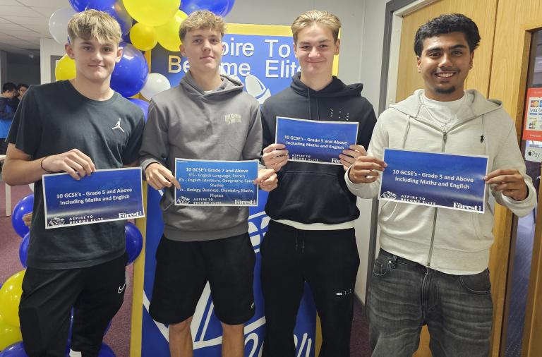 Four students stand in front of a balloon display holding up posters that show their results