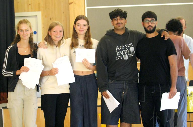 Five students stand in a row smiling with their results