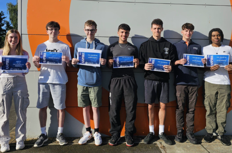 Seven students stand in a row smiling to the camerea and holding their results up