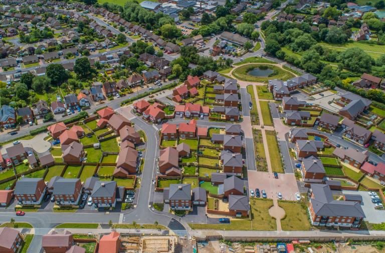 An aerial view of an area where new housing is being built, with large areas of green space and trees as well as parks with footpaths
