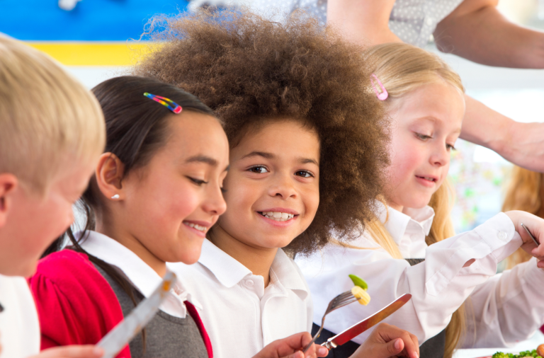 Four children in school uniform working at a table, one looking towards the camera smiling