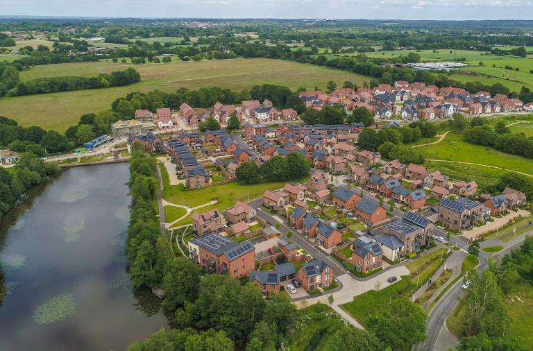 aerial view of new housing with an attractive lake surrounding it and open green space in the background