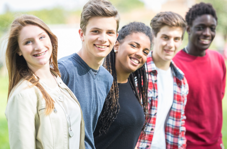 Five young people standing in a row smiling at the camera