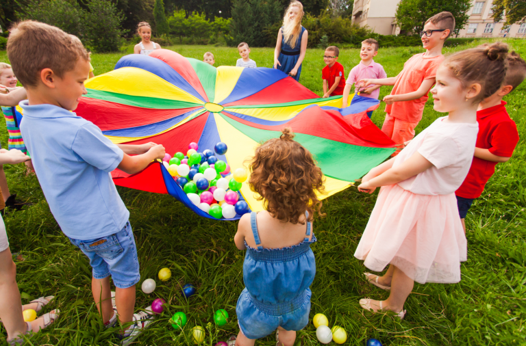 A group of children holding up a colourful parachute with balls balanced atop