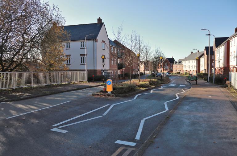 A section of the South Wokingham Distributor Road with a zebra crossing and beacons, surrounded by new houses and flats
