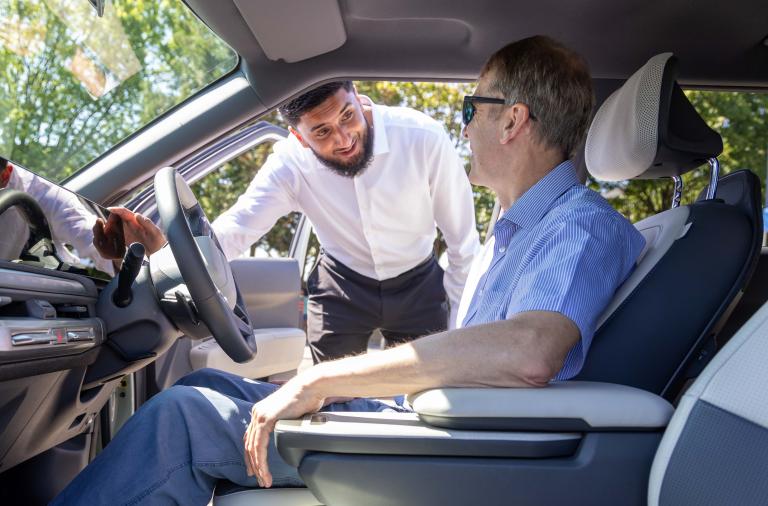 A salesman talks to a prospective customer sitting in the driver's seat of an electric vehicle