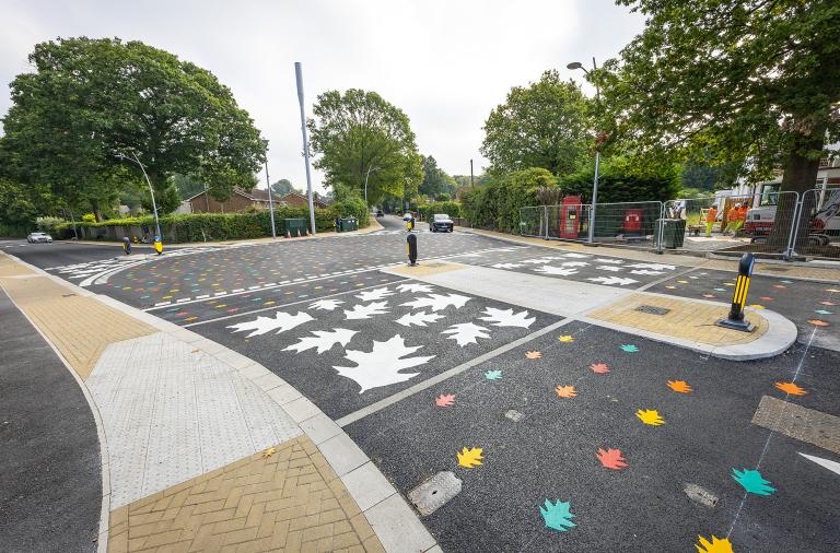 close up of crossing point at California Crossroads with white leaves painted on the road and a refuge island with bollards in the centre